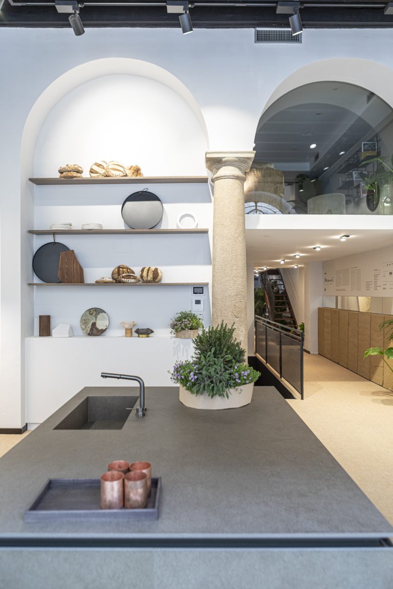 Maison de la Terre for Marie Claire Maison: kitchen island with a stone-effect top, open shelves of ceramics and arched windows.