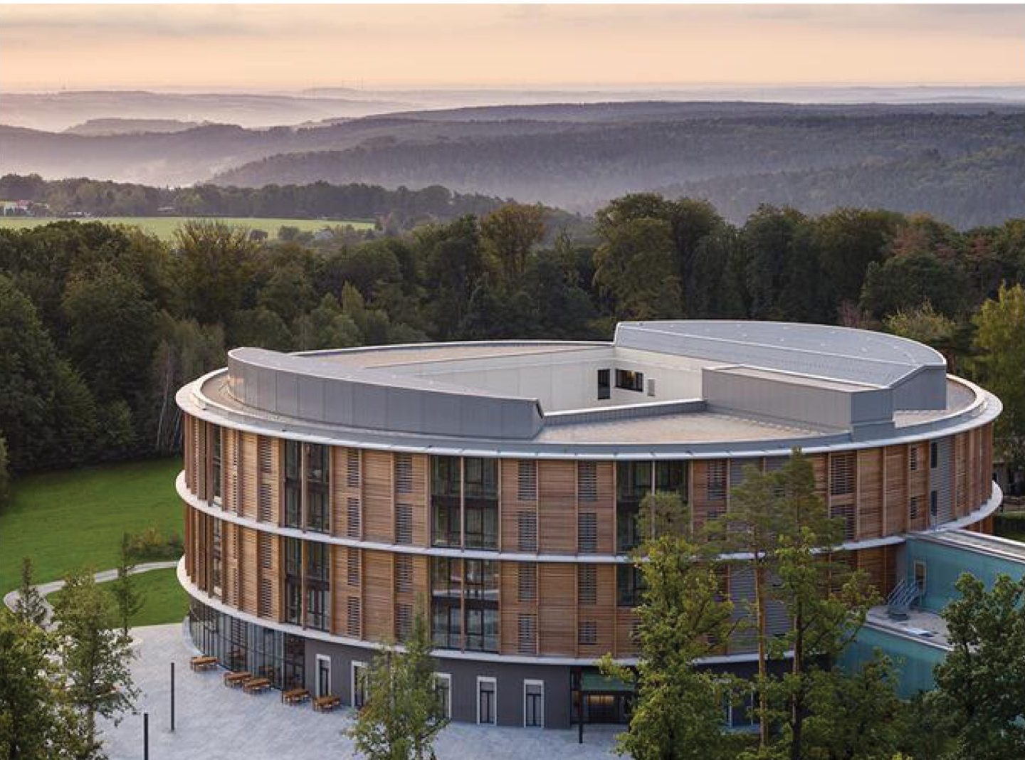 Waldkliniken Eisenberg: aerial view of the circular timber-clad hospital in wooded hills