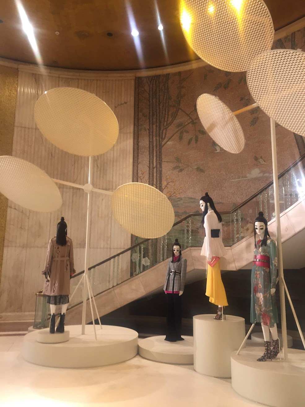 Zara installation for Milano Design Week: oversized mesh discs above mannequins on round plinths beside a staircase.
