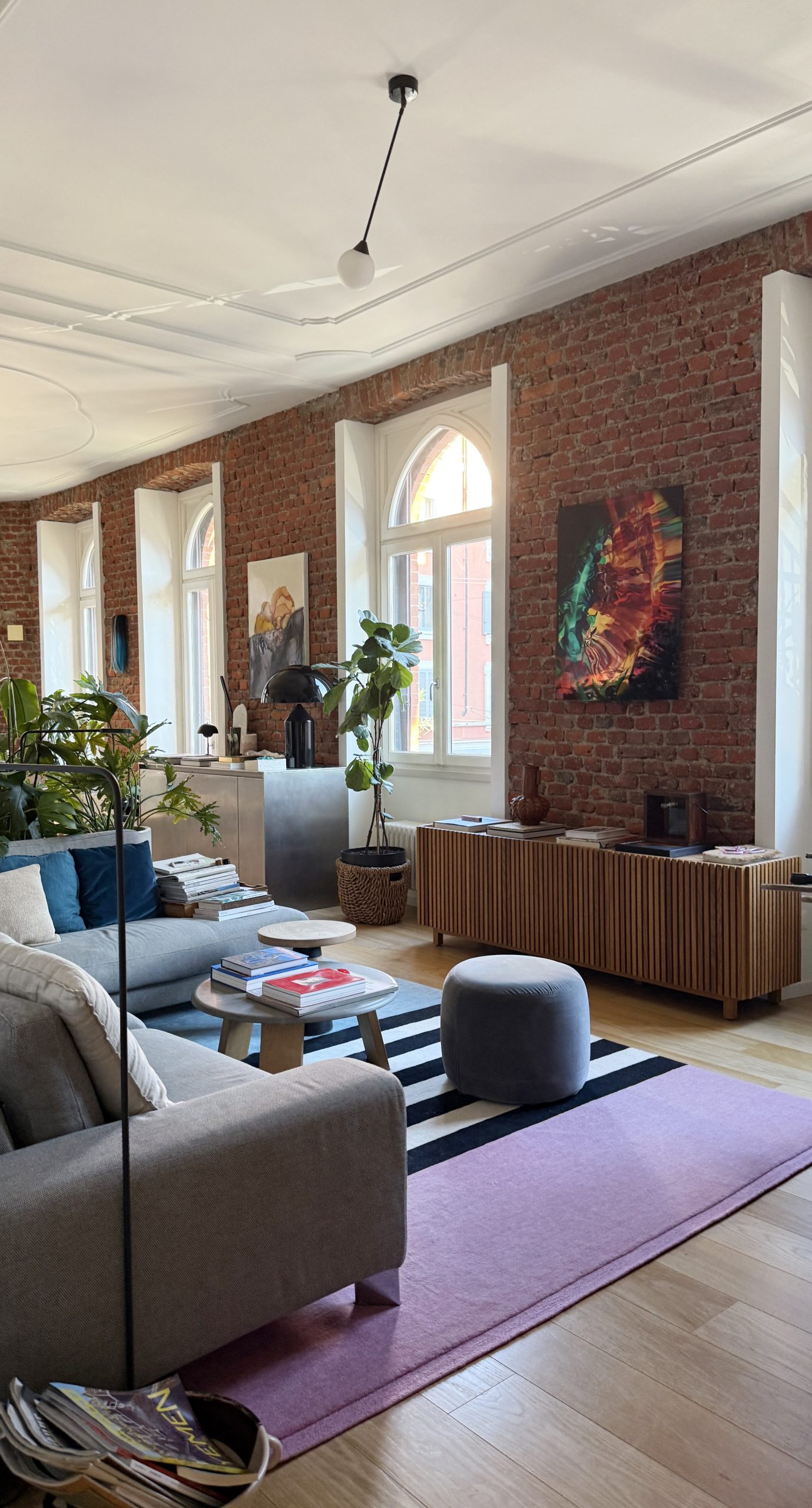 Living room of the Brick house in Milano with arched windows, exposed brick, a sofa and a purple rug.