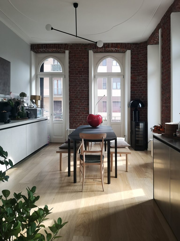 Kitchen and dining area of the Brick house in Milano with arched windows and a long wooden table.