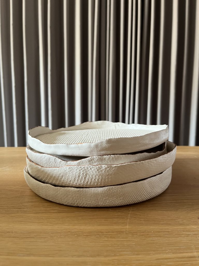 Stack of TESSUTI matte white ceramic plates inspired by furnishing fabrics.