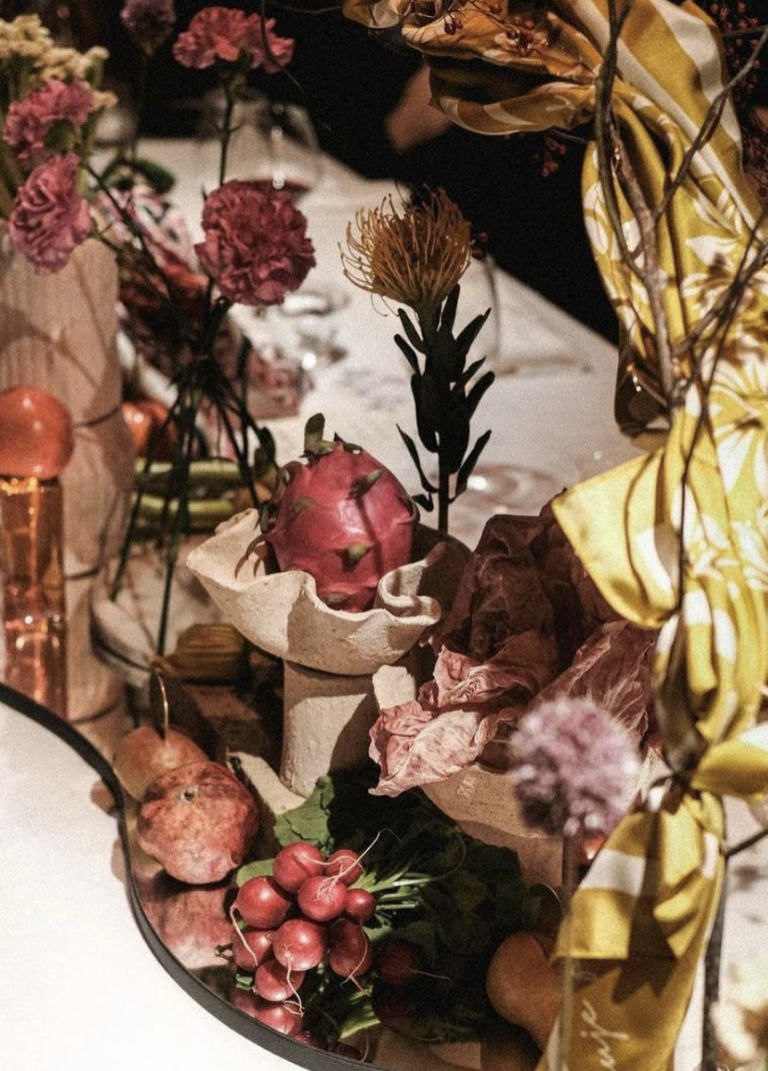 Event table centrepiece with flowers, pomegranates and ceramic vessels on a mirrored tray.