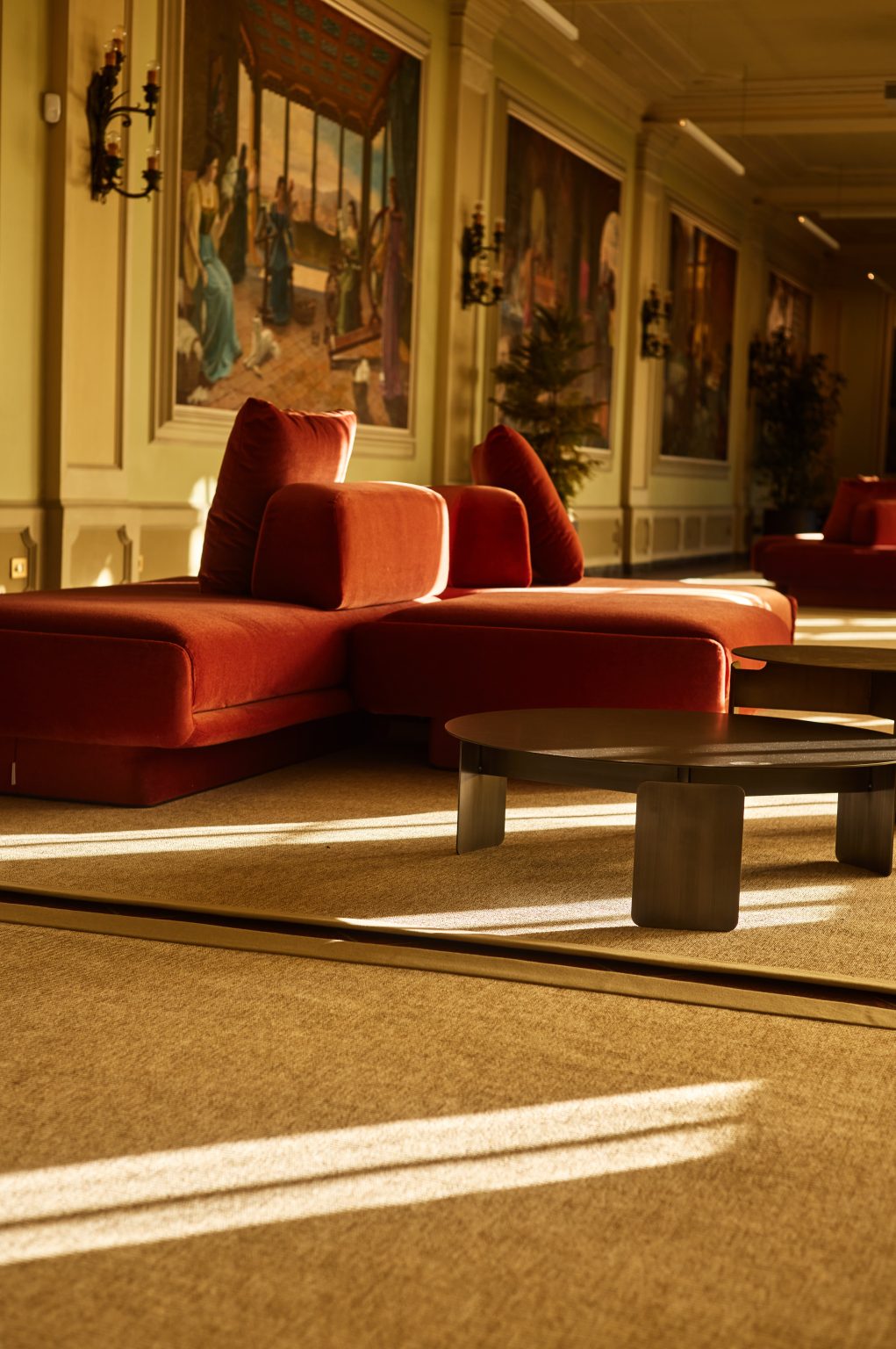 Sala quadri at Fondazione Zegna: rust velvet modular sofas and low round tables beneath large painted panels, interior design by Elena Pelosi.