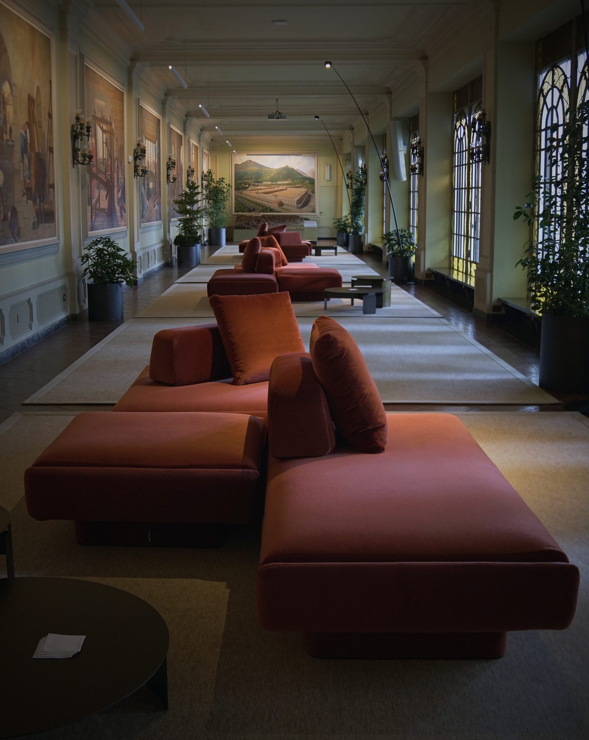 Perspective of the Sala quadri gallery at Fondazione Zegna, with rust velvet sofas, rugs and painted panels along the walls.