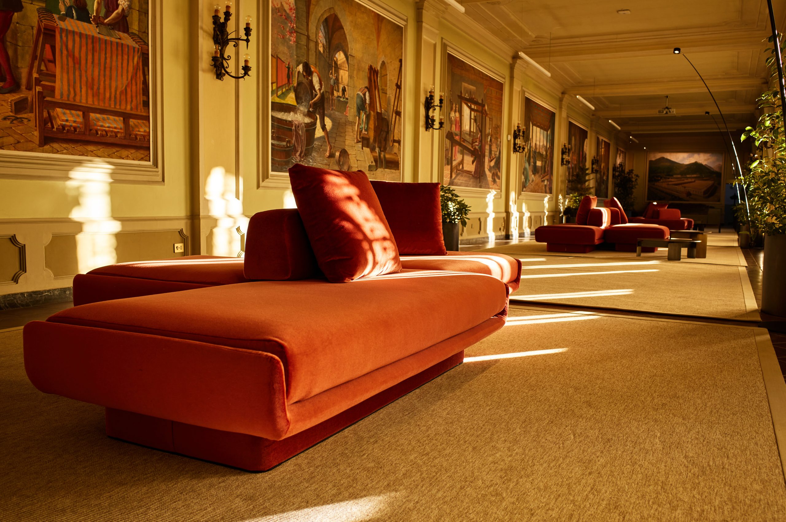 Rust velvet daybed in the Sala quadri at Fondazione Zegna, with painted panels lining the hall.