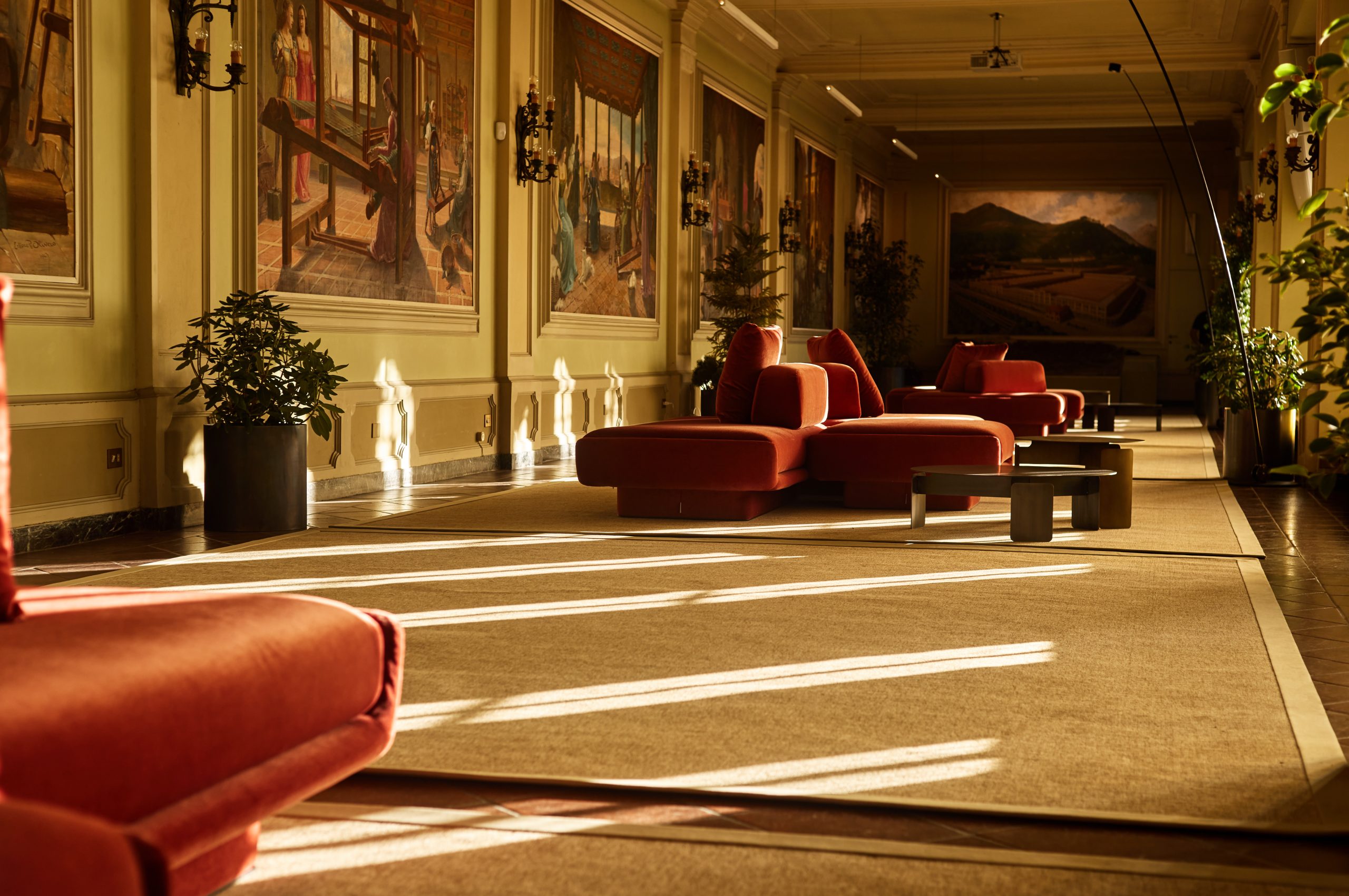 Sala quadri at Fondazione Zegna with groups of rust sofas, plants and rugs along the painted gallery.