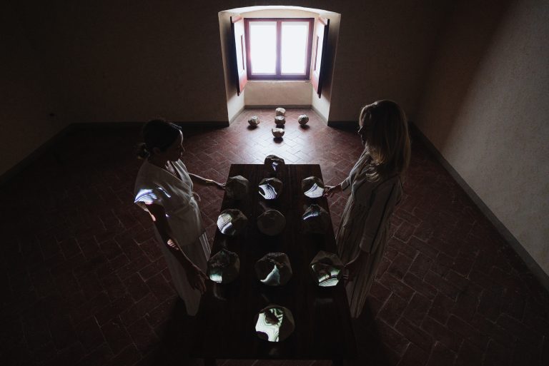 Portal of Memory performance, Villa Ferdinanda: two performers at a table of ceramic stones beneath a window