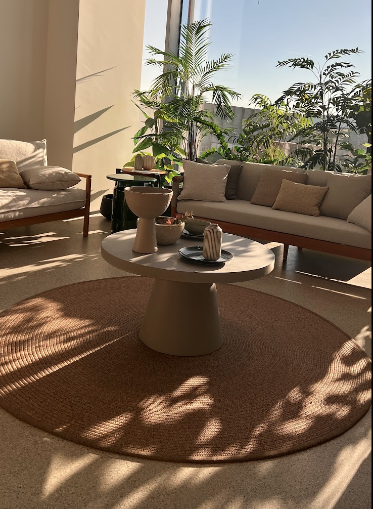 Interior of the Atmosphera Italy headquarters with outdoor sofas, a round table and a rug in a sunlit space.