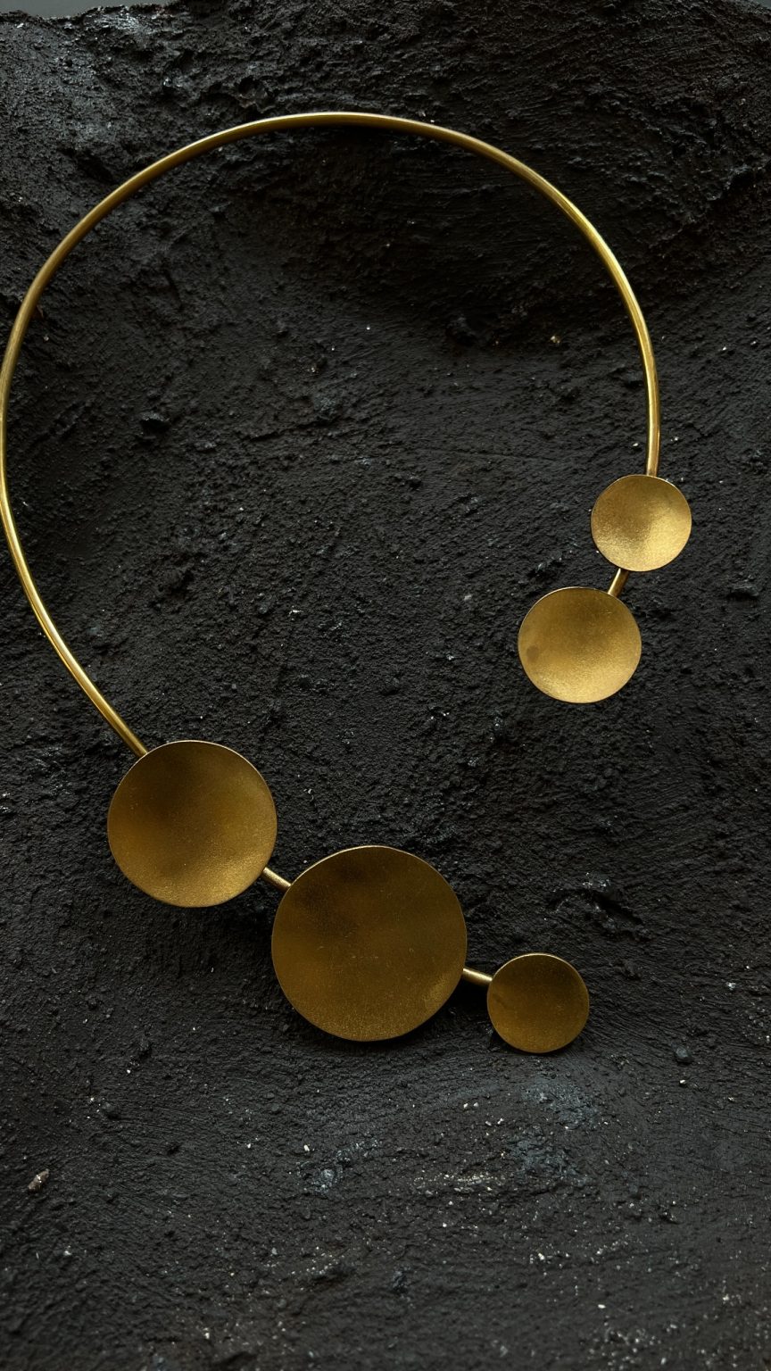 Cassiopea brass collar necklace with gold discs by Elena Pelosi, on dark stone.