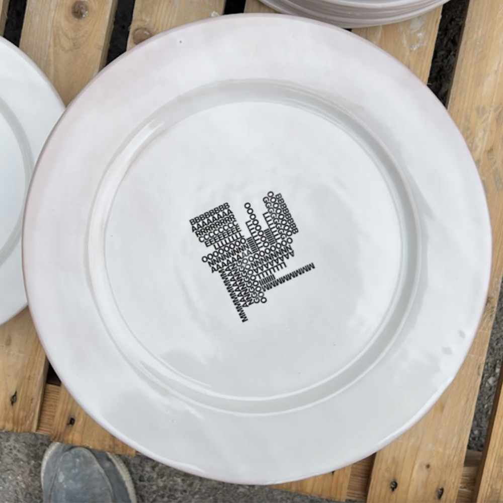 White ceramic plate with a black graphic motif on a wooden pallet, made for the Mango / Boglioli event.