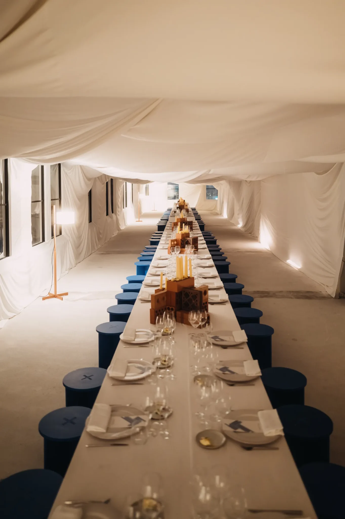 Long banquet table set with ceramic tableware under draped white fabric, the Mango / Boglioli dinner.