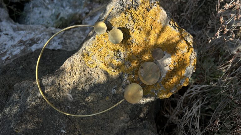Cassiopea brass necklace with gold discs resting on a lichen-covered rock.