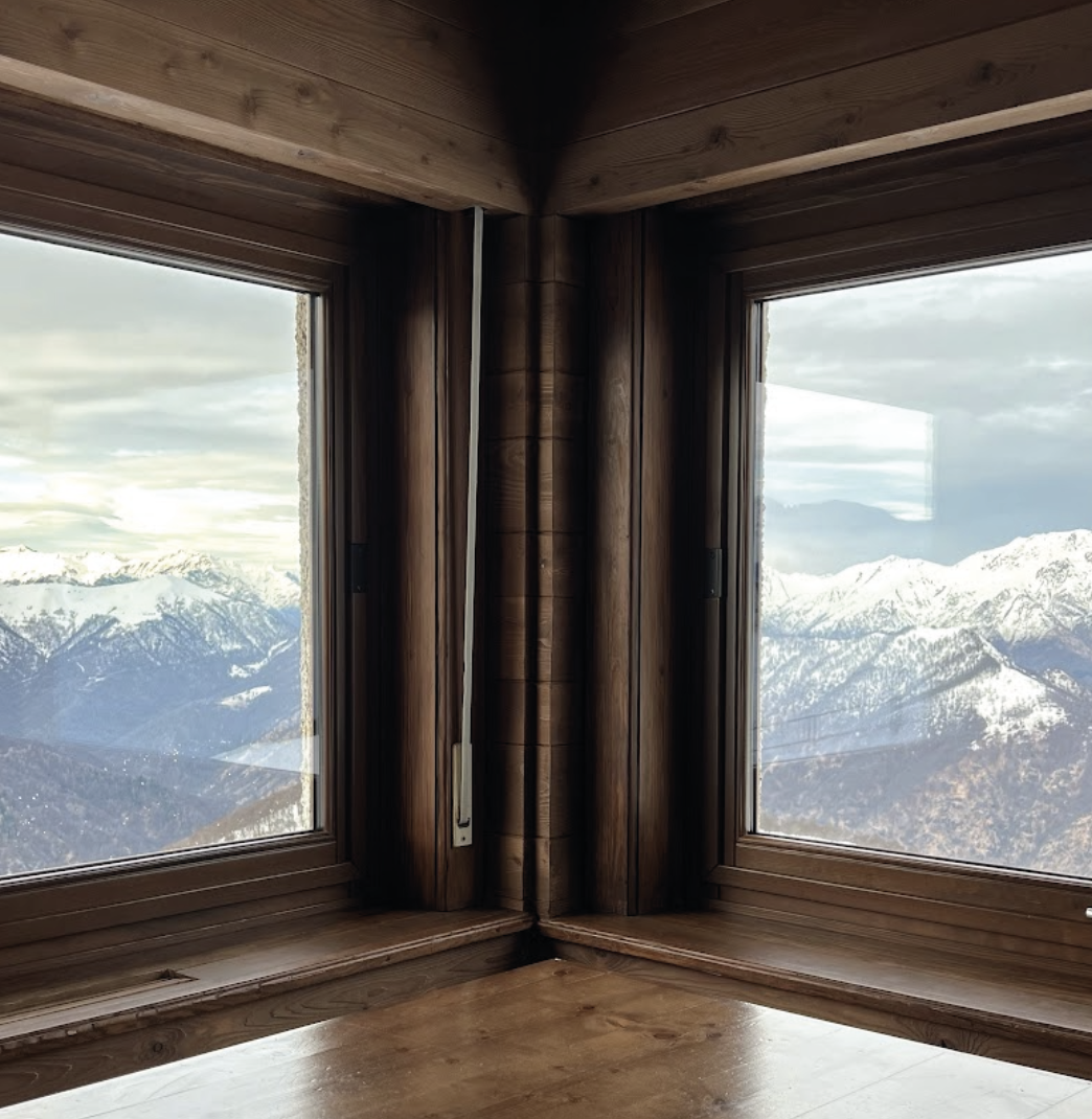 Finestra d’angolo del Rifugio Monte Marca con telai in legno e vista sulle vette alpine innevate, interior design di Elena Pelosi per Fondazione Zegna