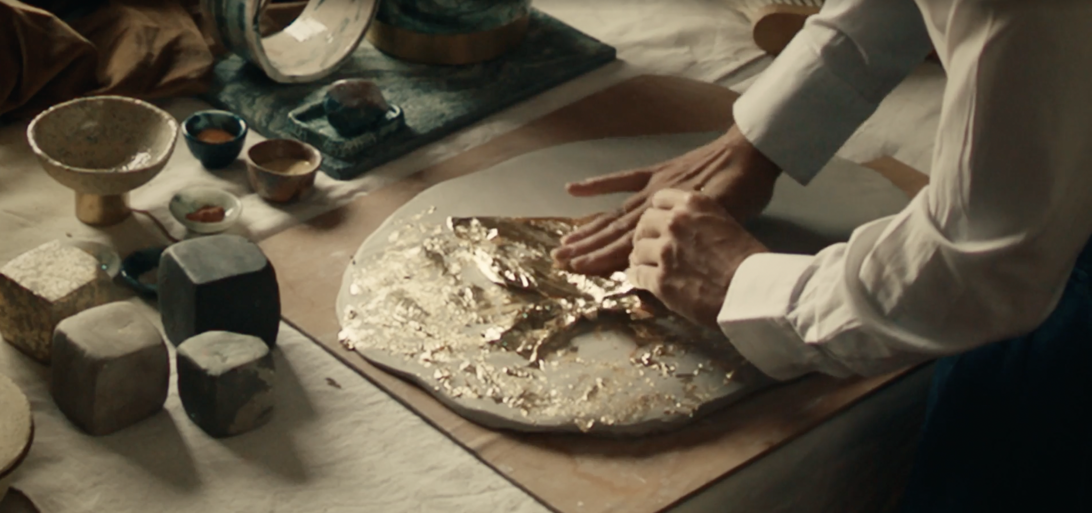 Hands pressing metallic leaf into a clay slab during the making of Elena Pelosi’s ceramic frames for Bvlgari Serpenti.