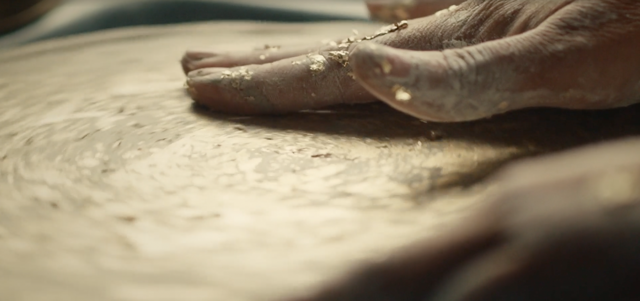 Close-up of a hand smoothing a clay slab flecked with metallic leaf, for Elena Pelosi’s Bvlgari Serpenti ceramic frames.