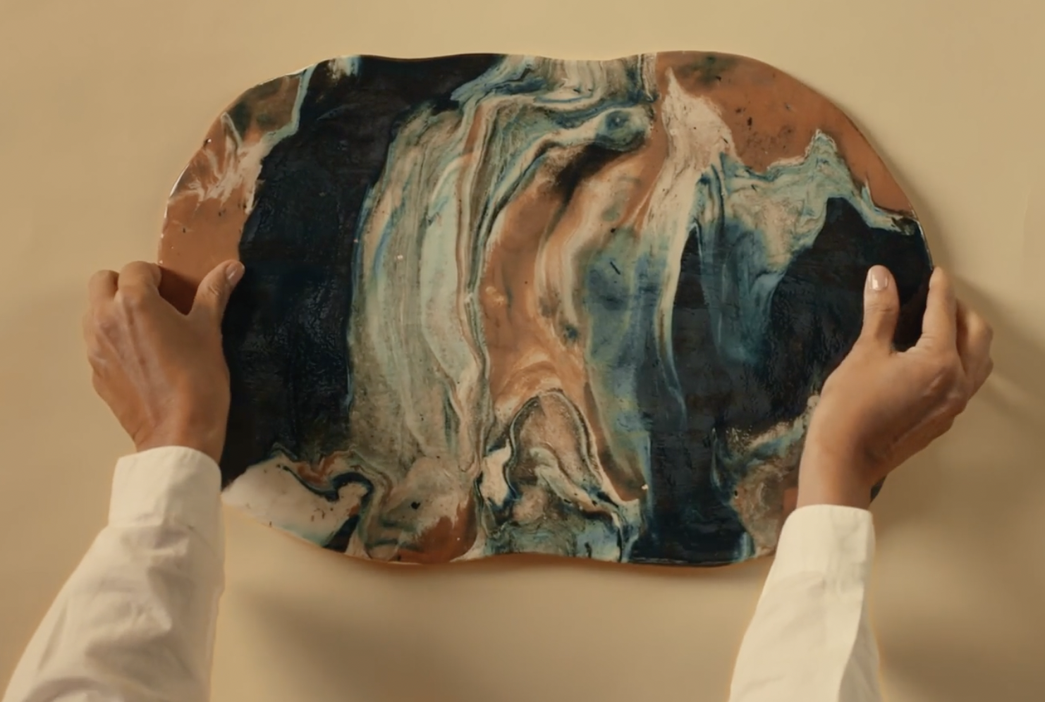 Hands holding a slab of artisanal marble made from reclaimed clays in blue, terracotta and white, by Elena Pelosi for Bvlgari.