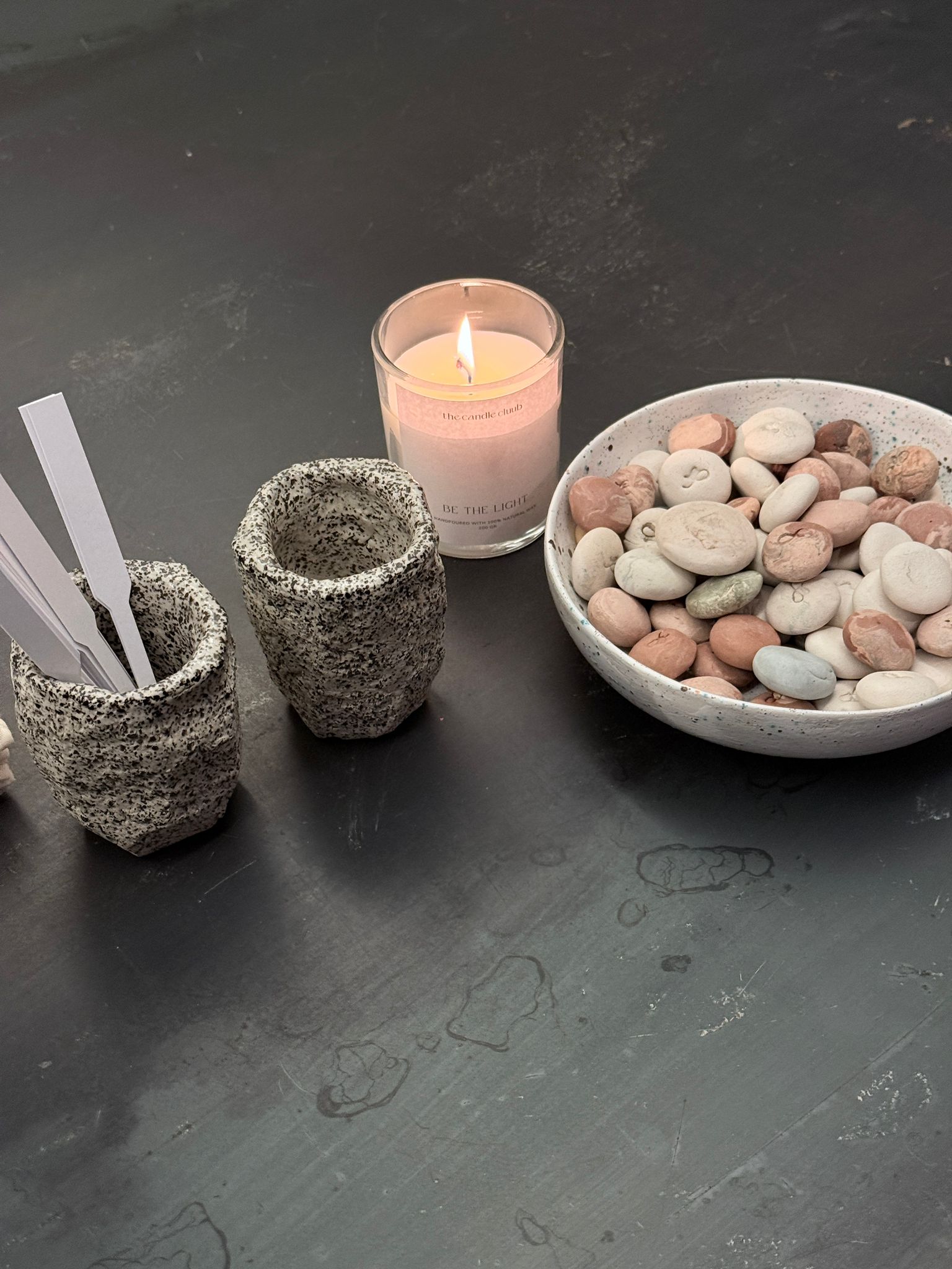 HABITARE event: candle, textured ceramic cups and a bowl of pebbles on a dark table