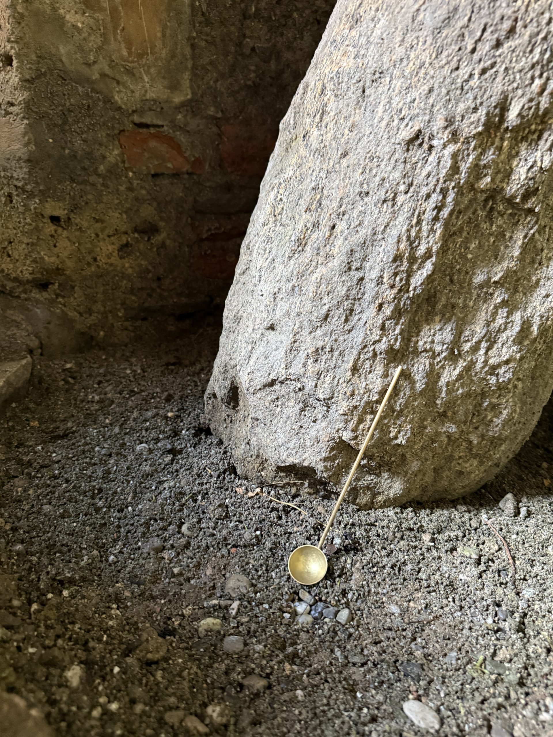 Mineralia homeware: brass ladle leaning against a boulder on gravel
