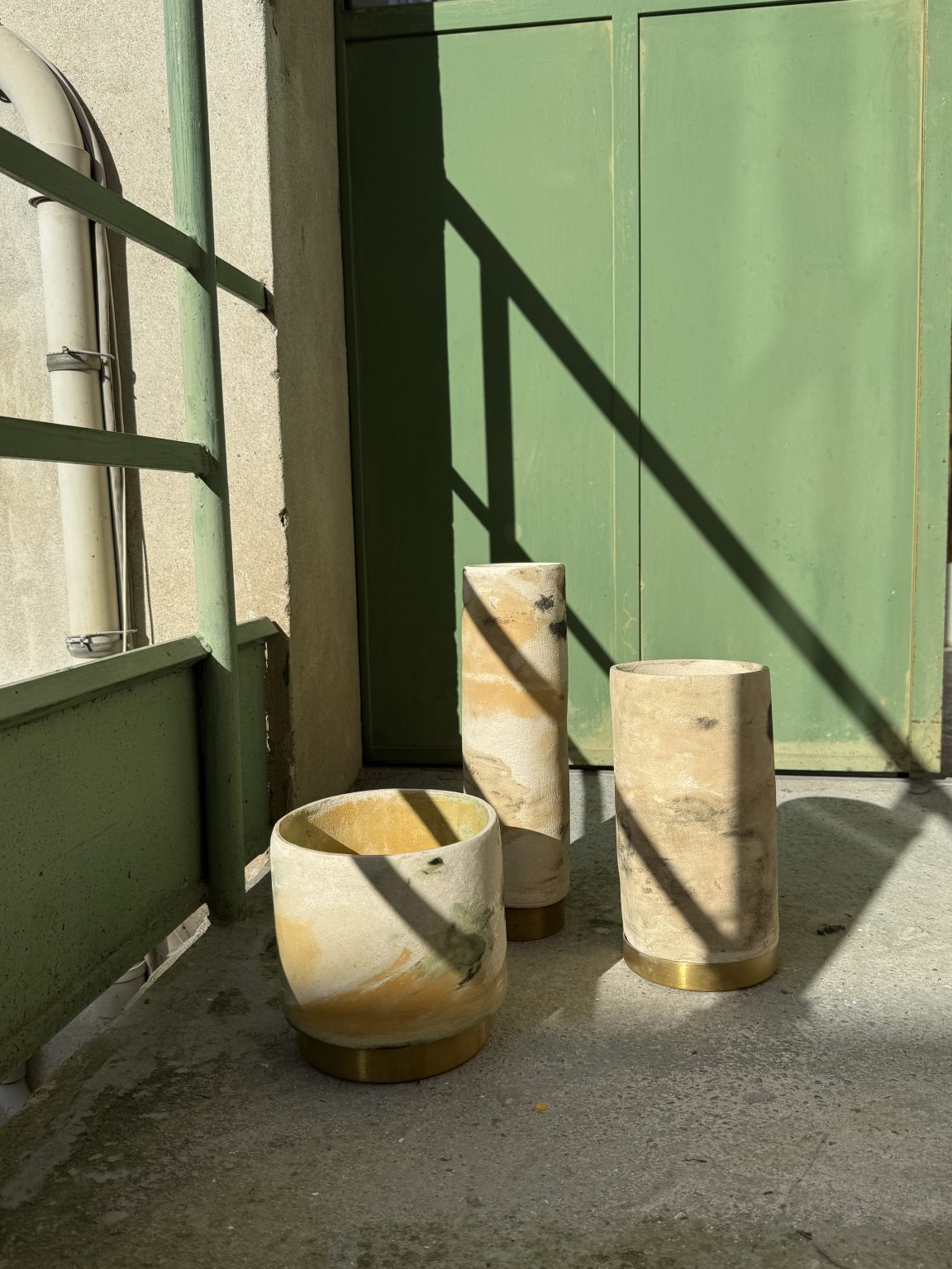 Panta Rei marbled ceramic vases with brass bases, made from recovered clays, on a concrete floor against a green wall.