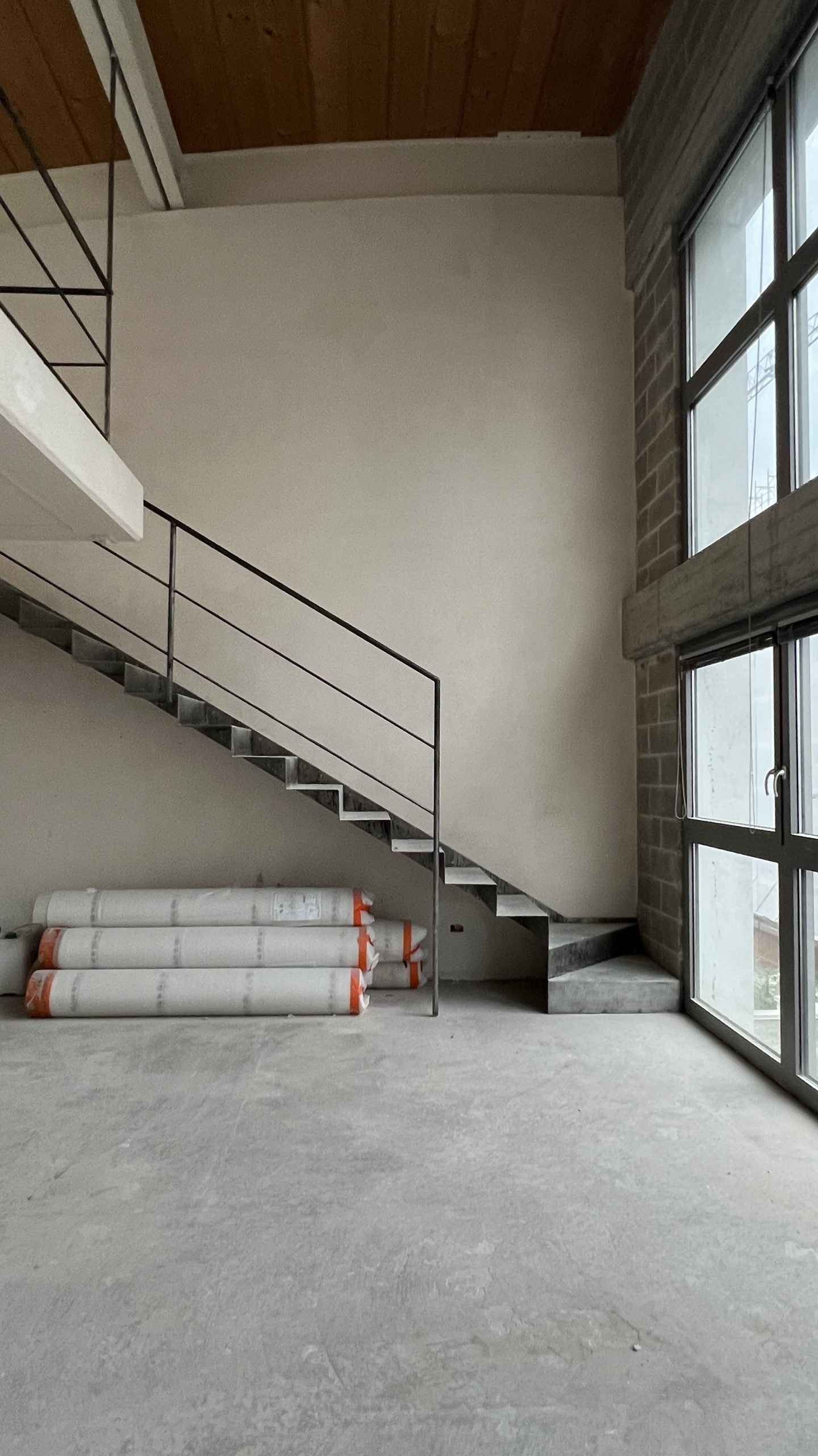 The Brutalist Grid: steel staircase and tall windows in the raw space during works