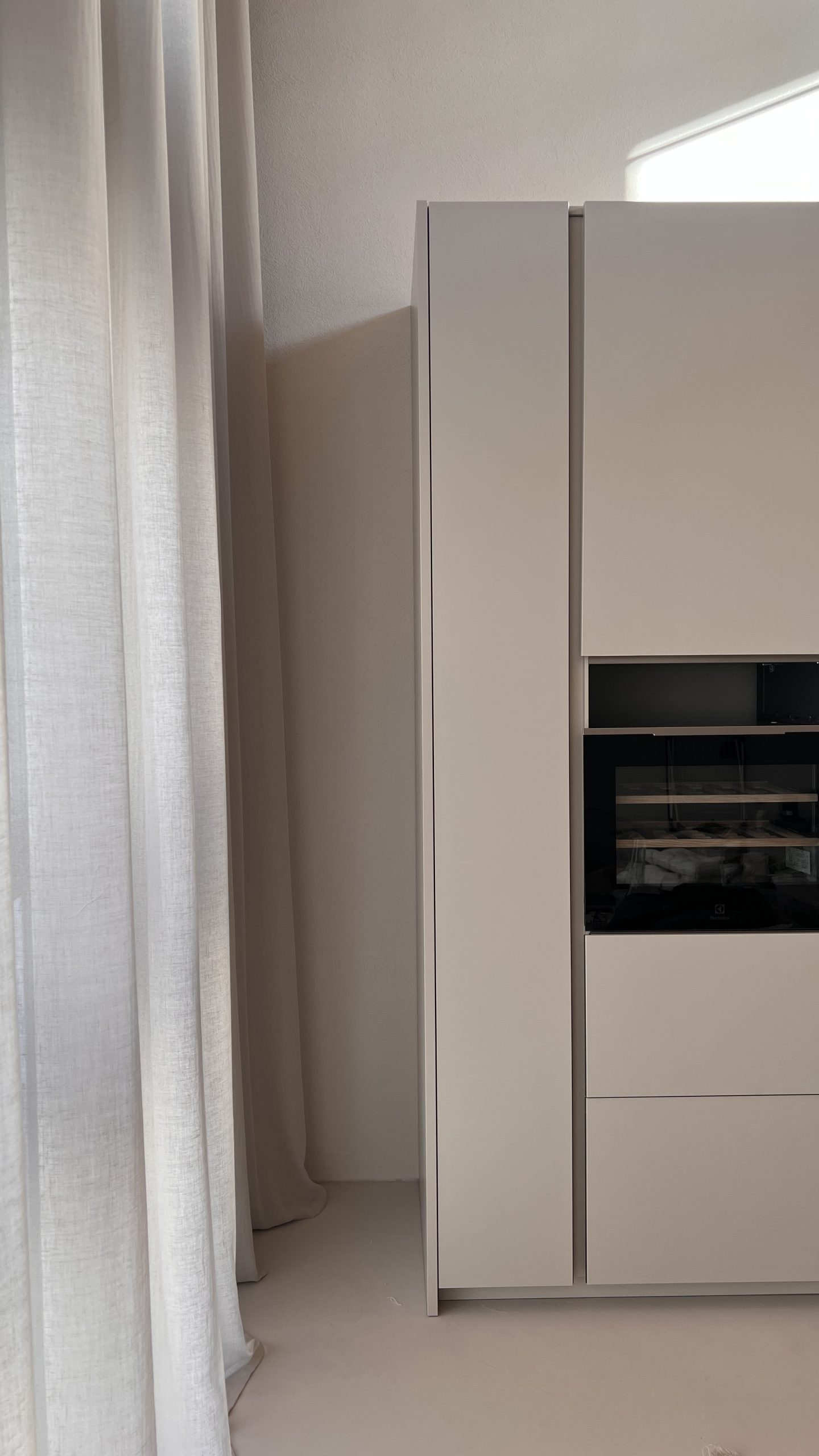 The Brutalist Grid: tall white kitchen units beside sheer curtains