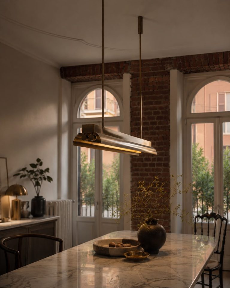 Linear Lamp 01 pendant light above a marble dining table in a room with arched windows and a brick wall.