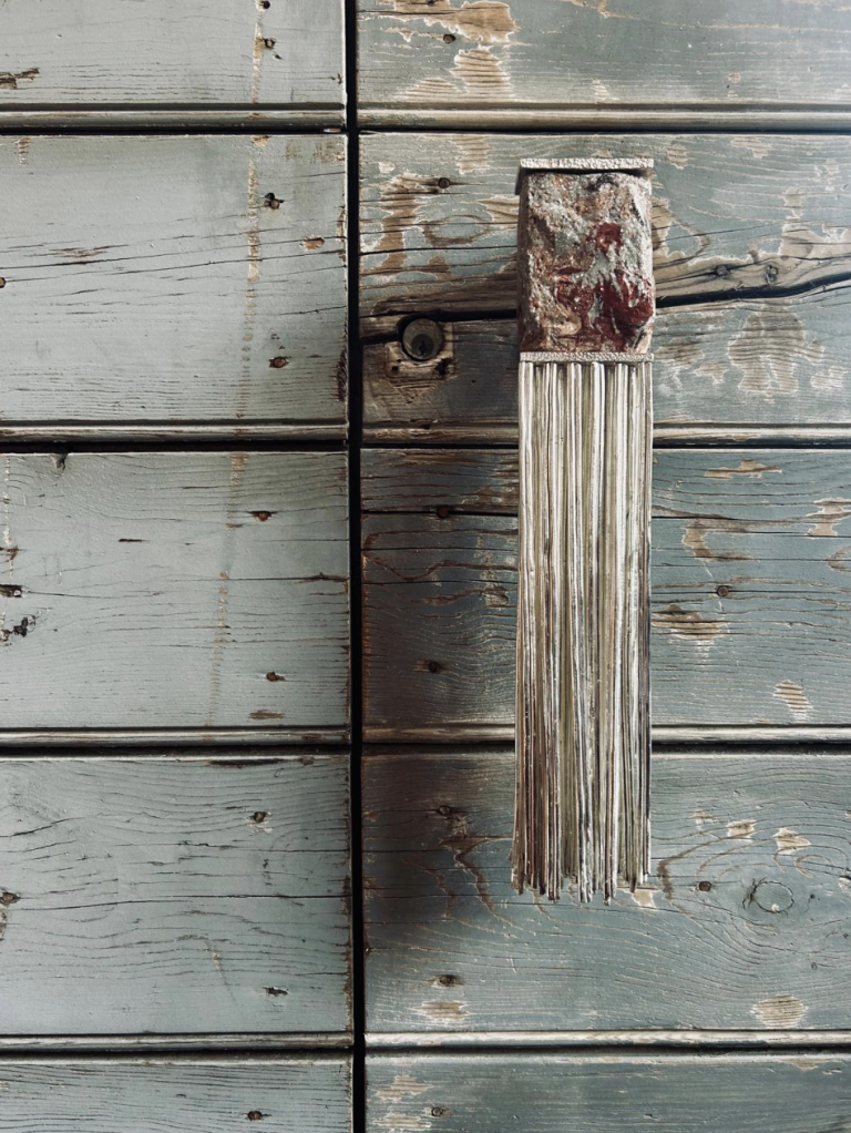 Memories handle by Elena Pelosi, a textured ceramic grip with a long fringe, on a weathered blue-green wooden door.
